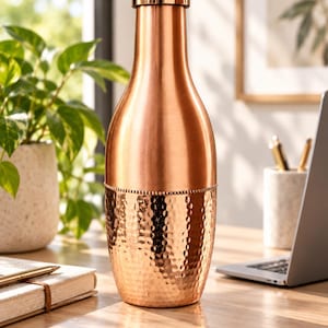 May include: A copper-colored metal bottle with a smooth, polished upper section and a textured, hammered lower section. The bottle features a cylindrical neck, a rounded body, and a matching metallic cap that seals the top of the vessel securely.