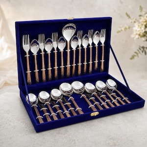 May include: A cutlery set featuring silver-toned bowls and tines with textured copper-coloured handles, presented in a rectangular blue velvet-lined storage case. The collection includes various forks, spoons, and a ladle arranged in slots.