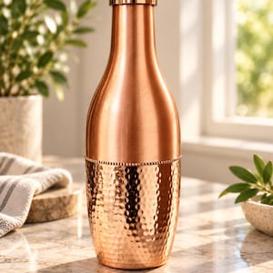 May include: A copper-colored metal water bottle with a smooth upper section and a hammered texture on the lower half. The bottle features a cylindrical shape, a narrow neck, and a matching metallic screw-top lid with a beaded detail at the center.