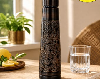 May include: A dark brown, cylindrical metal water bottle featuring an intricate, etched floral and paisley pattern in a lighter copper tone. The bottle has a matching screw-top lid and displays the text SSA SHIV SHAKTI ARTS in the top corner.