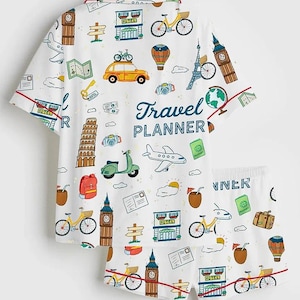 May include: White pajama set with a travel theme. The short-sleeved top and shorts feature a repeating pattern of travel icons, including bicycles, landmarks, and the text "Travel Planner". Red trim accents the edges.