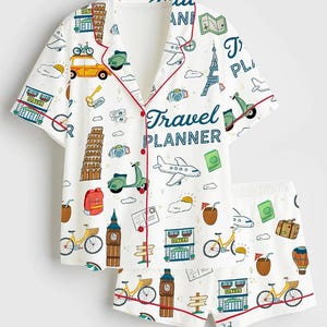 May include: White pajama set with a travel theme. The short-sleeved top and shorts feature a repeating pattern of travel icons, including bicycles, scooters, and landmarks. The top has red trim and the words "Travel Planner".
