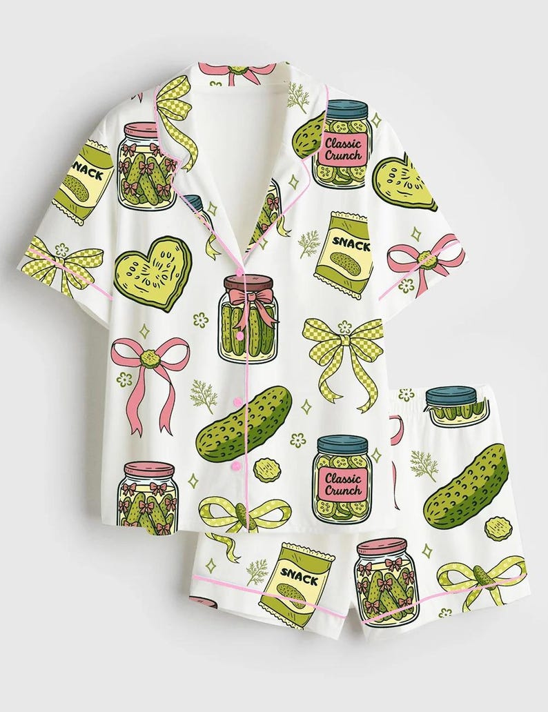 K&ouml;nnte beinhalten: Wei&szlig;es Pyjama-Set mit einem Gurkenmuster. Das Set besteht aus einem kurz&auml;rmeligen Hemd mit Kn&ouml;pfen und Shorts. Das Muster zeigt Gl&auml;ser mit Gurken, Gurkenscheiben, Schleifen und Snack-T&uuml;ten. Die Einfassung ist rosa.