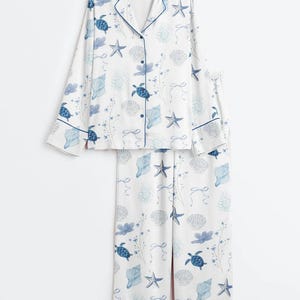 Peut inclure: Ensemble de pyjama blanc avec un motif bleu sur le th&egrave;me de la mer. Le haut &agrave; manches longues et le pantalon pr&eacute;sentent un motif r&eacute;p&eacute;t&eacute; de tortues, de coquillages et d'&eacute;toiles de mer. L'ensemble a des bordures et des boutons bleus.
