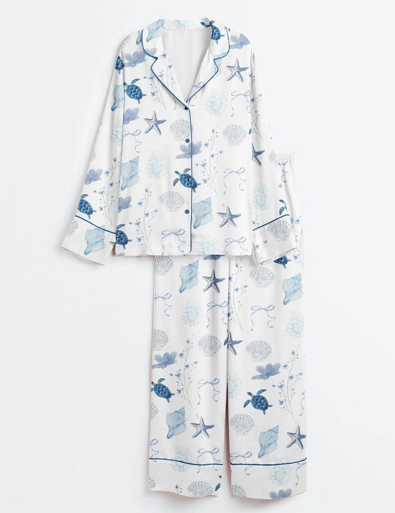 Peut inclure: Ensemble de pyjama blanc avec un motif bleu sur le th&egrave;me de la mer. Le haut &agrave; manches longues et le pantalon pr&eacute;sentent un motif r&eacute;p&eacute;t&eacute; de tortues, de coquillages et d'&eacute;toiles de mer. L'ensemble a des bordures et des boutons bleus.