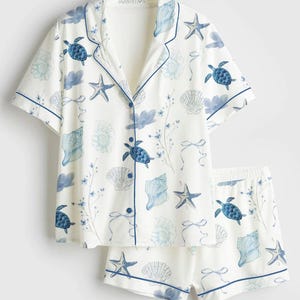Peut inclure: Ensemble de pyjama blanc avec un motif de vie marine bleu, comprenant des tortues, des coquillages et des &eacute;toiles de mer. Le haut &agrave; manches courtes et le short ont une bordure bleue. Le haut boutonn&eacute; a un col crant&eacute;.