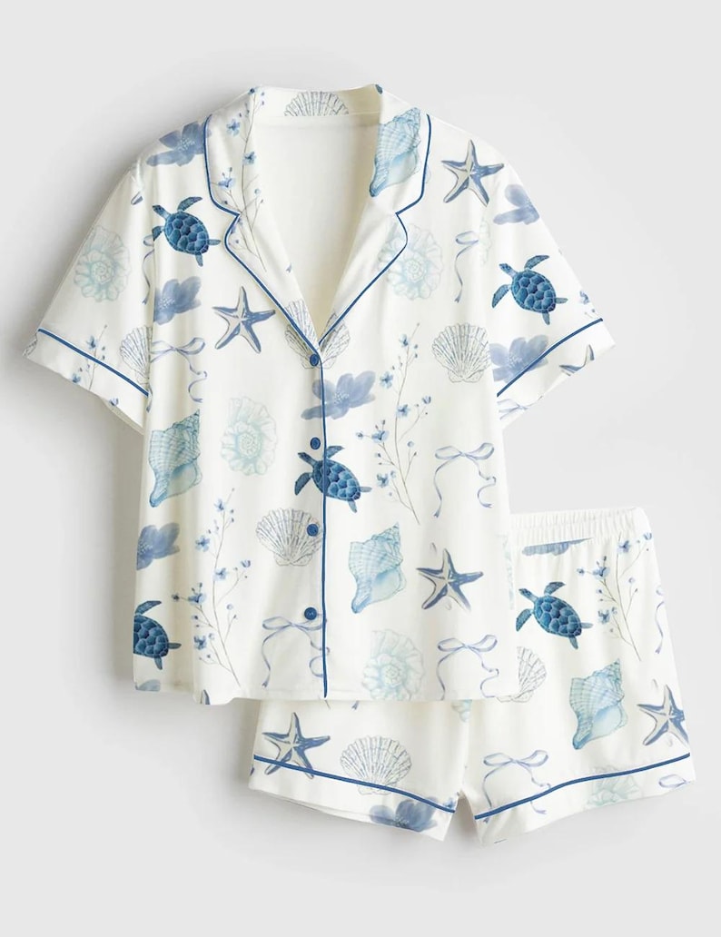 Peut inclure: Ensemble de pyjama blanc avec un motif de vie marine bleu, comprenant des tortues, des coquillages et des &eacute;toiles de mer. Le haut &agrave; manches courtes et le short ont une bordure bleue. Le haut boutonn&eacute; a un col crant&eacute;.