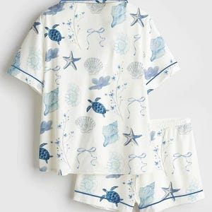 Peut inclure: Ensemble de pyjama blanc avec un motif de coquillages et de tortues bleues. Le haut &agrave; manches courtes et le short ont une bordure bleue. Le motif comprend des &eacute;toiles de mer, des coquillages et des accents floraux.