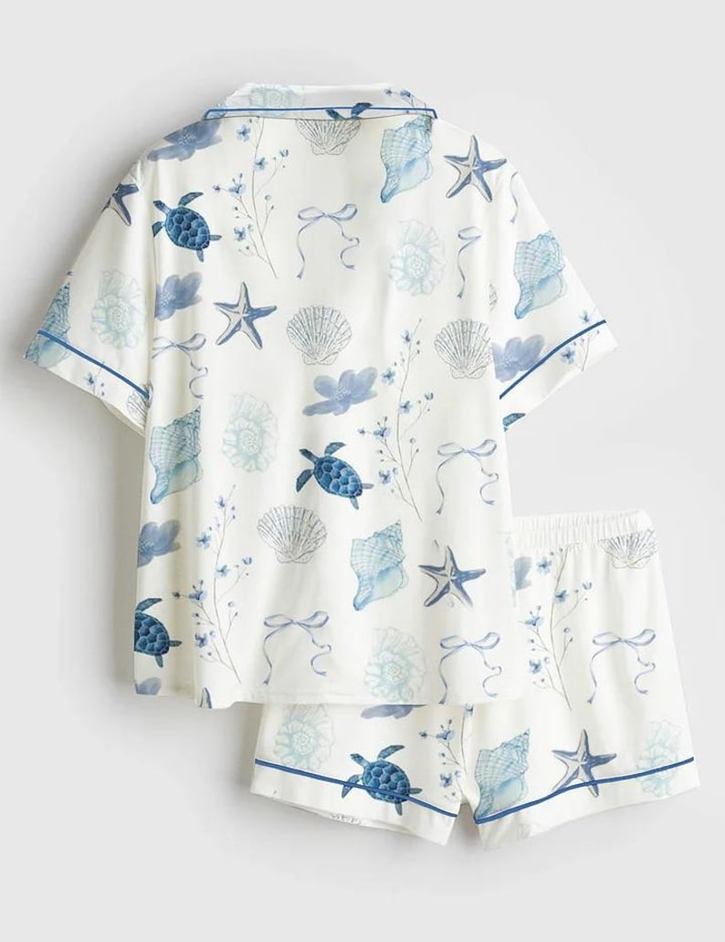 Peut inclure: Ensemble de pyjama blanc avec un motif de coquillages et de tortues bleues. Le haut &agrave; manches courtes et le short ont une bordure bleue. Le motif comprend des &eacute;toiles de mer, des coquillages et des accents floraux.