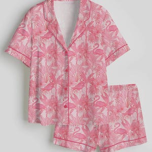 K&ouml;nnte beinhalten: Rosa Pyjama-Set mit Flamingo- und tropischem Bl&auml;ttermuster. Das kurz&auml;rmelige Oberteil hat eine Knopfleiste und einen Reverskragen. Die Shorts haben einen passenden Aufdruck und eine rosa Paspelierung. Hergestellt aus weichem, leichtem Stoff.