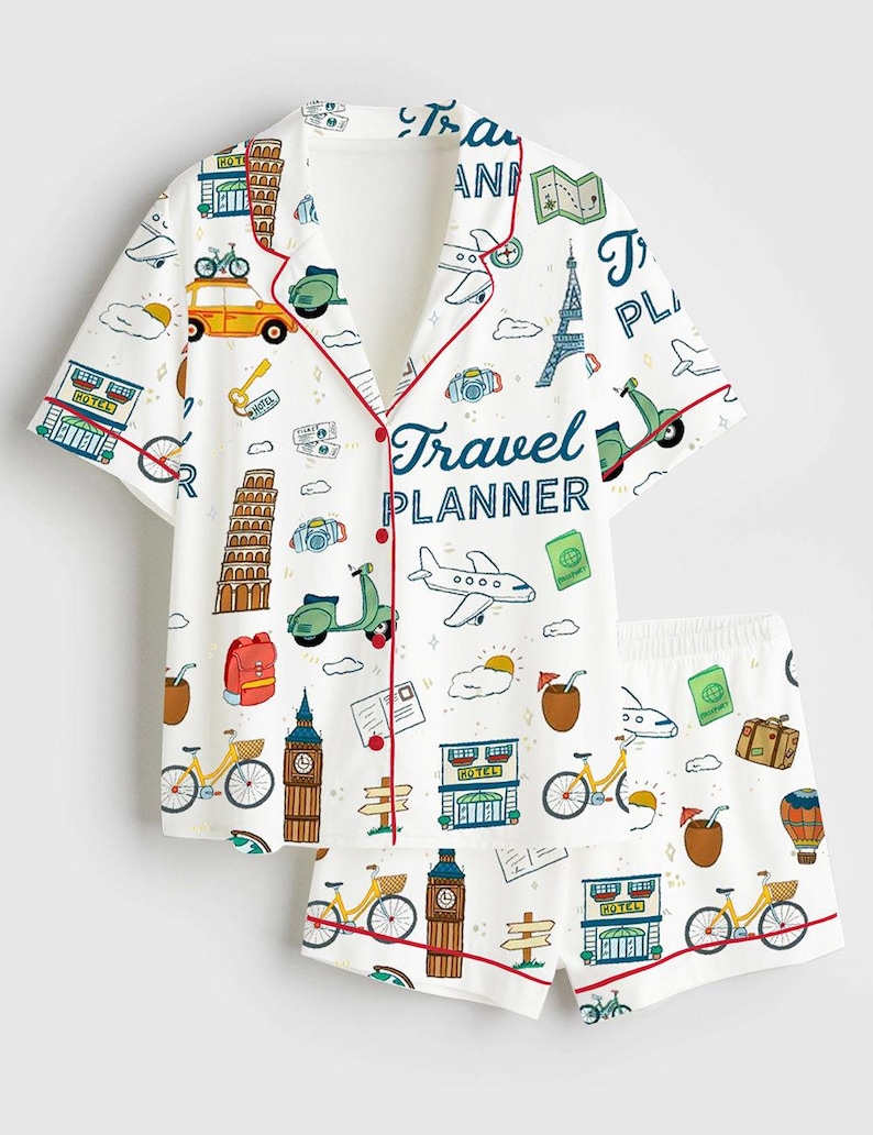 May include: White pajama set with a travel theme. The short-sleeved top and shorts feature a repeating pattern of travel icons, including bicycles, landmarks, and the text "Travel Planner". Red trim accents the edges.