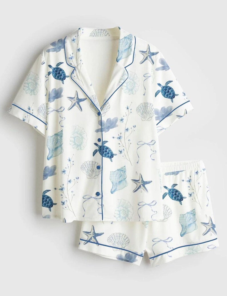 Peut inclure: Ensemble de pyjama blanc avec un motif de vie marine bleu. Le haut &agrave; manches courtes et le short pr&eacute;sentent des tortues de mer bleues, des coquillages et des &eacute;toiles de mer. Les bords sont bord&eacute;s d'une fine bordure bleue.