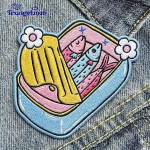May include: Embroidered patch featuring a sardine can design. The patch has a light blue border, a pink interior, and a yellow lid. Three colorful fish are inside. Two white flowers are on the sides. The text "Texasgirl2026" is at the top.