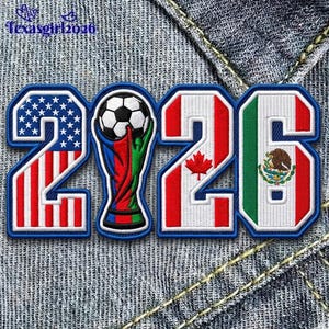 May include: An embroidered patch featuring the number 2026, where the 2 is styled with the United States flag, the 0 is a soccer trophy, the 2 is the Canadian flag with a maple leaf, and the 6 is the Mexican flag with its central emblem.