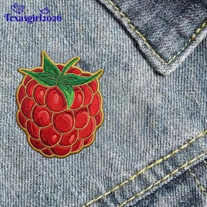 May include: An embroidered patch shaped like a red raspberry with green leaves, featuring a gold border. The patch is placed on blue denim fabric with visible yellow stitching. The text texasgirl2026 is printed in blue in the top left corner.