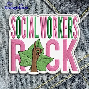 May include: Embroidered patch with the text "SOCIAL WORKERS ROCK" in pink and green. The letter "R" is replaced with a hand gesture and a green leaf. The patch is white with a stitched border, set against a denim background.