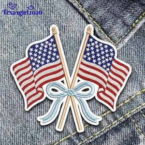 May include: Embroidered patch featuring two American flags crossed with a light blue bow. The flags have red and white stripes and a blue field with white stars. The patch is on a denim background.