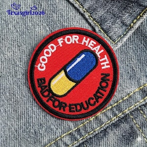 May include: A round, red embroidered patch with the text "GOOD FOR HEALTH BAD FOR EDUCATION" in white. A blue and yellow capsule is in the center. The patch is on a denim jacket.