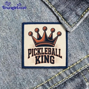 May include: A square patch with a navy blue border features a crown design with pickleball-like spheres. The words "PICKLEBALL KING" are in bold, stylized lettering. The patch is set against a denim background.