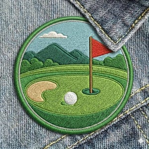 May include: Embroidered patch featuring a golf course scene. The design includes a green, a sand trap, a golf ball, a red flag, and a blue sky with a cloud. The patch is round with a green border and is set against a denim background.