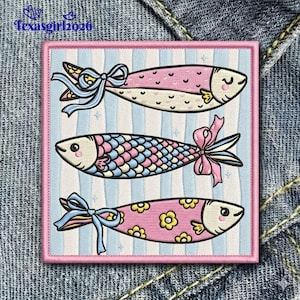 May include: Embroidered patch featuring three whimsical fish designs. The fish are in pink, blue, and yellow, each with a bow. The background is striped in light blue and pink, with the text "Texasgirl2026" in the upper left corner.