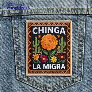 May include: Embroidered patch with the words "CHINGA LA MIGRA" in white on a black background, featuring a central orange flower, cacti, and other colorful flowers. The patch is bordered in brown and is sewn onto a denim jacket pocket.