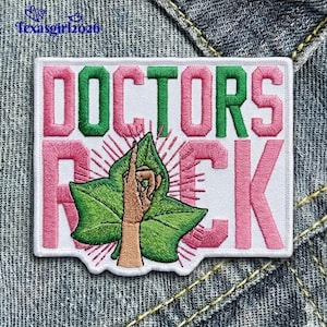 May include: Embroidered patch with the words "DOCTORS ROCK" in pink and green. A green leaf with a hand pointing upwards is in the center. The patch is on a white background with a white border.