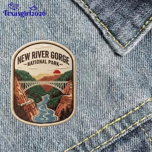 May include: An embroidered patch featuring the New River Gorge National Park with a large arched bridge spanning a river between rocky cliffs under a red sun. The text New River Gorge National Park is stitched in black on a cream background.