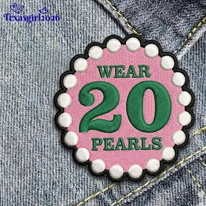 May include: A pink patch with the words "WEAR 20 PEARLS" in green, surrounded by white pearl-like beads and a black border. The patch is on a denim background.