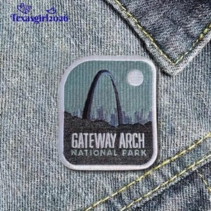 May include: A square patch featuring the Gateway Arch National Park. The patch has a light blue background with a depiction of the arch, a cityscape, and a moon. The text "GATEWAY ARCH NATIONAL PARK" is displayed.