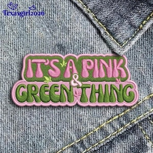 May include: Embroidered patch with the text "IT'S A PINK & GREEN THING" in pink and green. The patch is on a denim background. The text is in a bubble-style font with a pink outline and green fill.