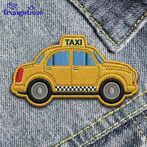 May include: Embroidered yellow taxi patch with black tires, blue windows, and a checkered pattern along the bottom. The word "TAXI" is displayed on the roof. The patch is sewn onto a denim background.