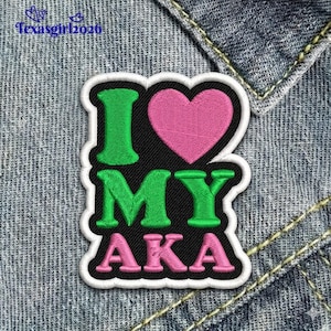 May include: Embroidered patch with the text "I MY AKA" in green and pink, with a pink heart. The patch has a black background and a white border, set against a denim background.