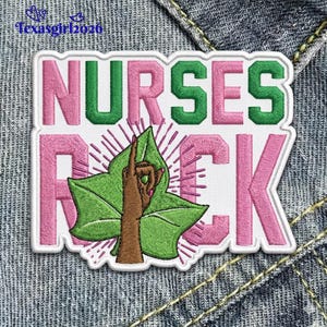 May include: Embroidered patch with the words "NURSES ROCK" in pink and green. The patch features a green leaf with a brown hand making a gesture. The patch is on a denim background.