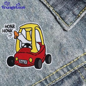 May include: Embroidered patch featuring a red and yellow toy car with a white goose driver. The patch has the word "SILLY" on the car and "HONK HONK" above it. The patch is on a denim background.