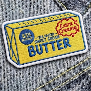 May include: Embroidered patch featuring a yellow butter package design with blue and red text. The patch reads "BUTTER" in large blue letters, with details like "83% Butterfat", "Sea Salted Sweet Cream", and "Extra Creamy".