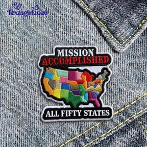 May include: A colorful embroidered patch featuring a map of the United States with each state in a different color. The patch has the words "MISSION ACCOMPLISHED" and "ALL FIFTY STATES" in bold text.