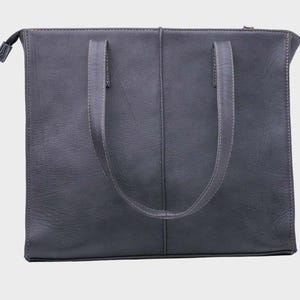 May include: A charcoal gray leather tote bag with a rectangular shape and a zipper closure. The bag features two handles and a vertical seam down the center. The stitching is a lighter gray color.
