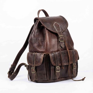 May include: A brown leather backpack with multiple pockets and adjustable straps. The backpack features a flap closure with a buckle and a drawstring top. The leather has a distressed look, and the stitching is visible.