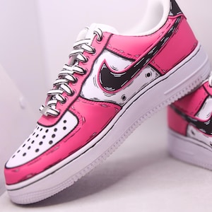 Peut inclure: Une paire de baskets basses présentant un coloris rose vif et blanc avec des contours noirs marqués créant une esthétique de bande dessinée. Les chaussures comprennent des lacets blancs avec des accents noirs, un swoosh Nike noir et une semelle en caoutchouc blanc.