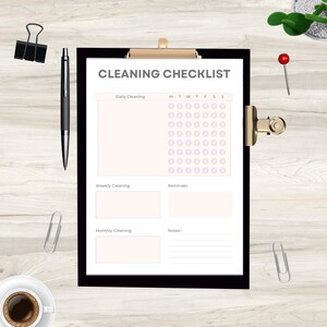Op de afbeelding: Een zwart klembord met een witte schoonmaakchecklist met secties voor dagelijkse, wekelijkse en maandelijkse schoonmaak, herinneringen en notities. Een zwarte pen, paperclips en een rode punaises zijn ook aanwezig op de afbeelding.