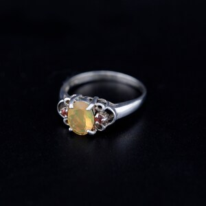 Peut inclure: Une bague en argent avec une pierre d'opale ovale et deux petites pierres rouges sur la bande.
