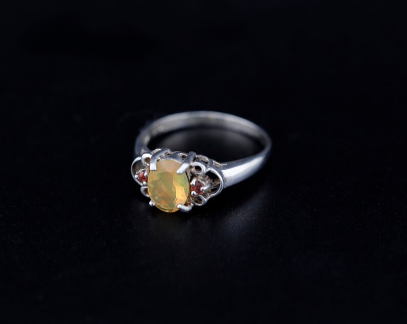 Peut inclure: Une bague en argent avec une pierre d'opale ovale et deux petites pierres rouges sur la bande.