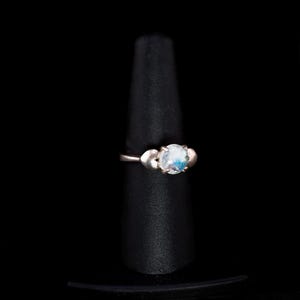 May include: A silver ring with a round, iridescent gemstone surrounded by two smaller silver hearts.