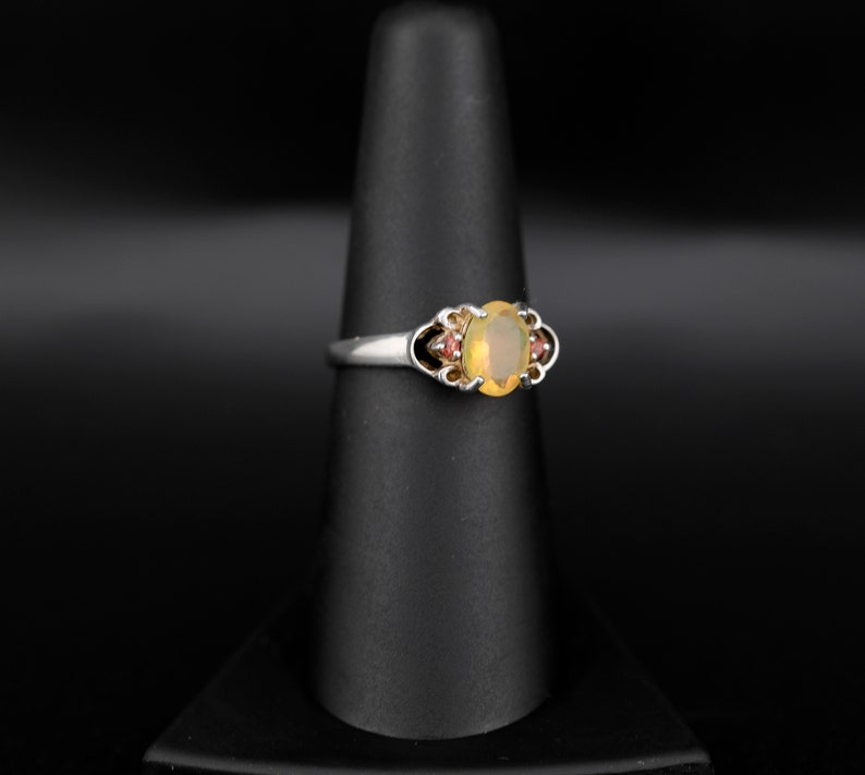 Peut inclure: Une bague en argent avec une opale ovale et deux petites pierres rouges de chaque c&ocirc;t&eacute;.