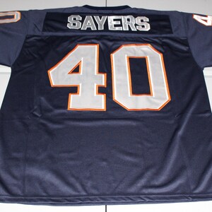 May include: Navy blue football jersey with the name "SAYERS" across the shoulders and the number "40" on the front and sleeves. The numbers and letters are white with orange trim. Orange stripes accent the sleeves.