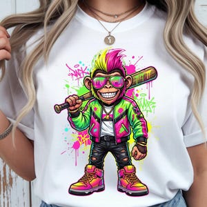 May include: White t-shirt featuring a cartoon monkey with sunglasses, a baseball bat, and a colorful jacket. The monkey has a mohawk and is surrounded by graffiti-style paint splatters. The design is vibrant and eye-catching.