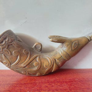 May include: A carved wooden powder horn with a hand-shaped design. The horn is brown with intricate floral and leaf carvings. It features a loop for hanging and is set against a red surface.