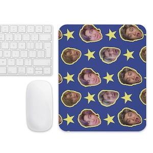 Könnte beinhalten: Ein blaues Mauspad mit einem Muster aus Gesichtern und gelben Sternen. Eine weiße Tastatur und Maus befinden sich links. Das Mauspad ist rechteckig mit abgerundeten Ecken.