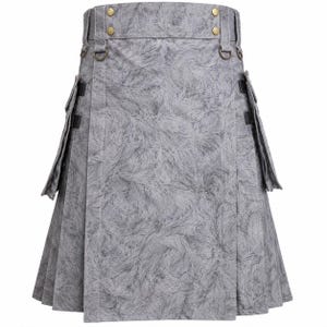 May include: A grey kilt featuring a textured, swirling pattern throughout the fabric. The garment includes a high waistband with four brass-colored buttons, two side cargo pockets with black straps, and metal D-rings attached at the waist.